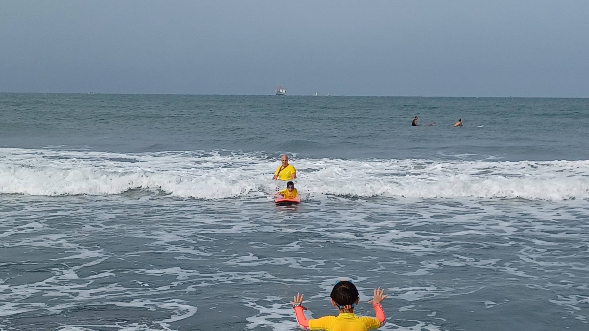 A child surfing in the prone position. Coach in the background. Child in the foreground